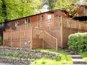 image of acorn bank lodge on Fallbarrow Park, surrounded on two sides with decking and with mature trees behind