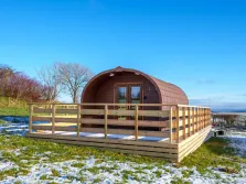 This image shows a glamping pod near Penrith on a raised deck surrounded by fencing. It is winter and there is a little snow on the ground. 
