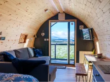 This image shows the inside of a pod near Penrith for glamping in the lake district, with a timber ceiling and a bed and couch. Through the open doors we can see the north pennine fells