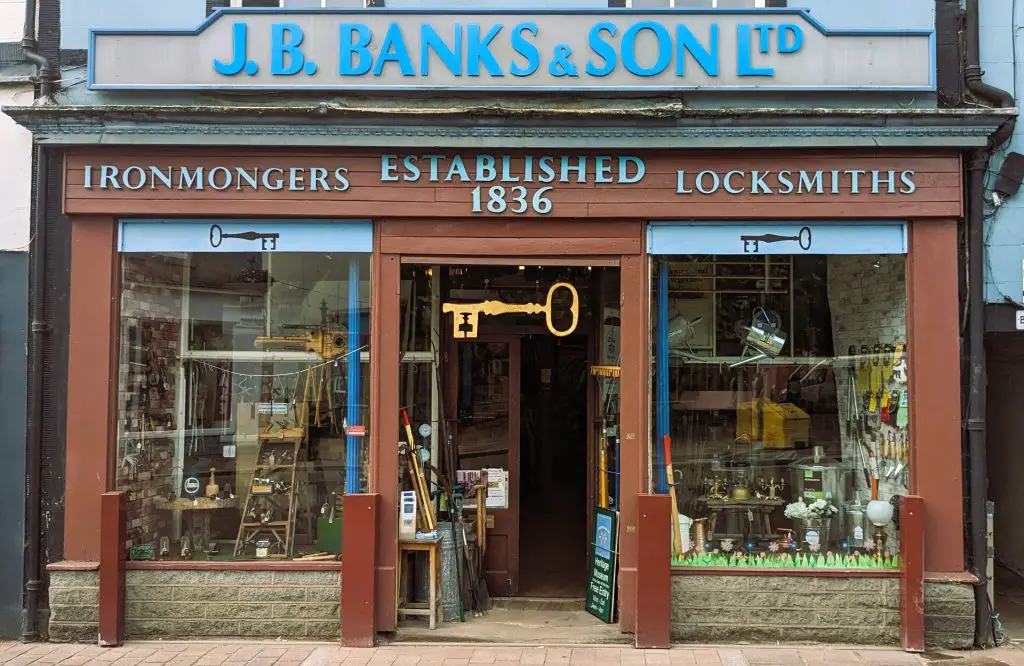 Image of the exterior of J.B. Banks and sons Iron mongers, photo shows the shop front with lots of wares in the windows and a large key decoration hanging in the doorway
