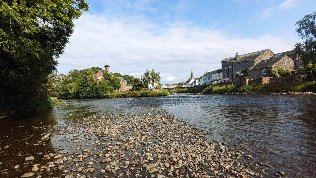 Image of the confluence of the rivers Cocker and Derwent. you can see the two rivers meeting in the centre of the image. trees line the left side and house on the right