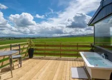 Image of a lodge in the Eden valley, photo shows deck, fence, hot tub, clouds and a blue sky