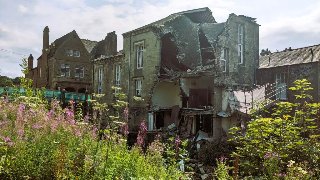 Image of the exterior of the old courthouse building. the building has partially collapsed flower can be seen in the foreground