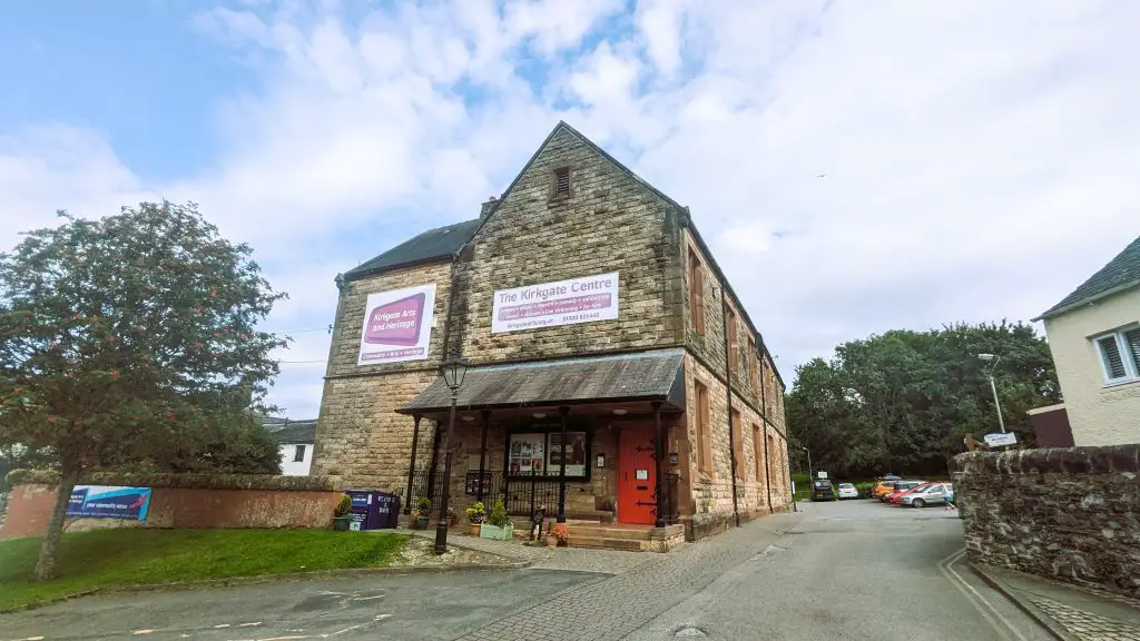 Image of the Kirkgate Centre, a large building in center of the image with a car park to the right and tree to the left and blue sky