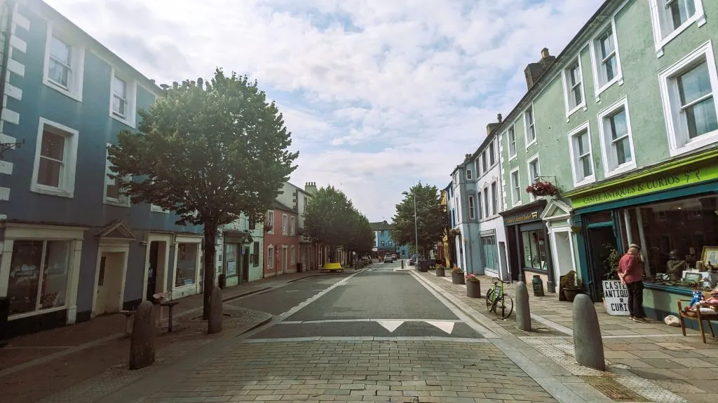 image of Marketplace in Cockermouth. rows of buildings, shops and trees run down both sides of the street. the sky is blue with some clouds.