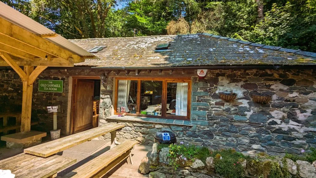 Image of the old sawmill tearooms next to bassenthwaite lake. photo shows stone building and benches with trees in the background