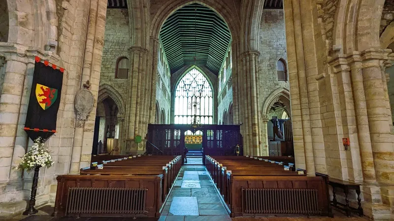 image of the interior of the Cartmel Priory, photo shows the big stained glass window from the inside as well as the pews